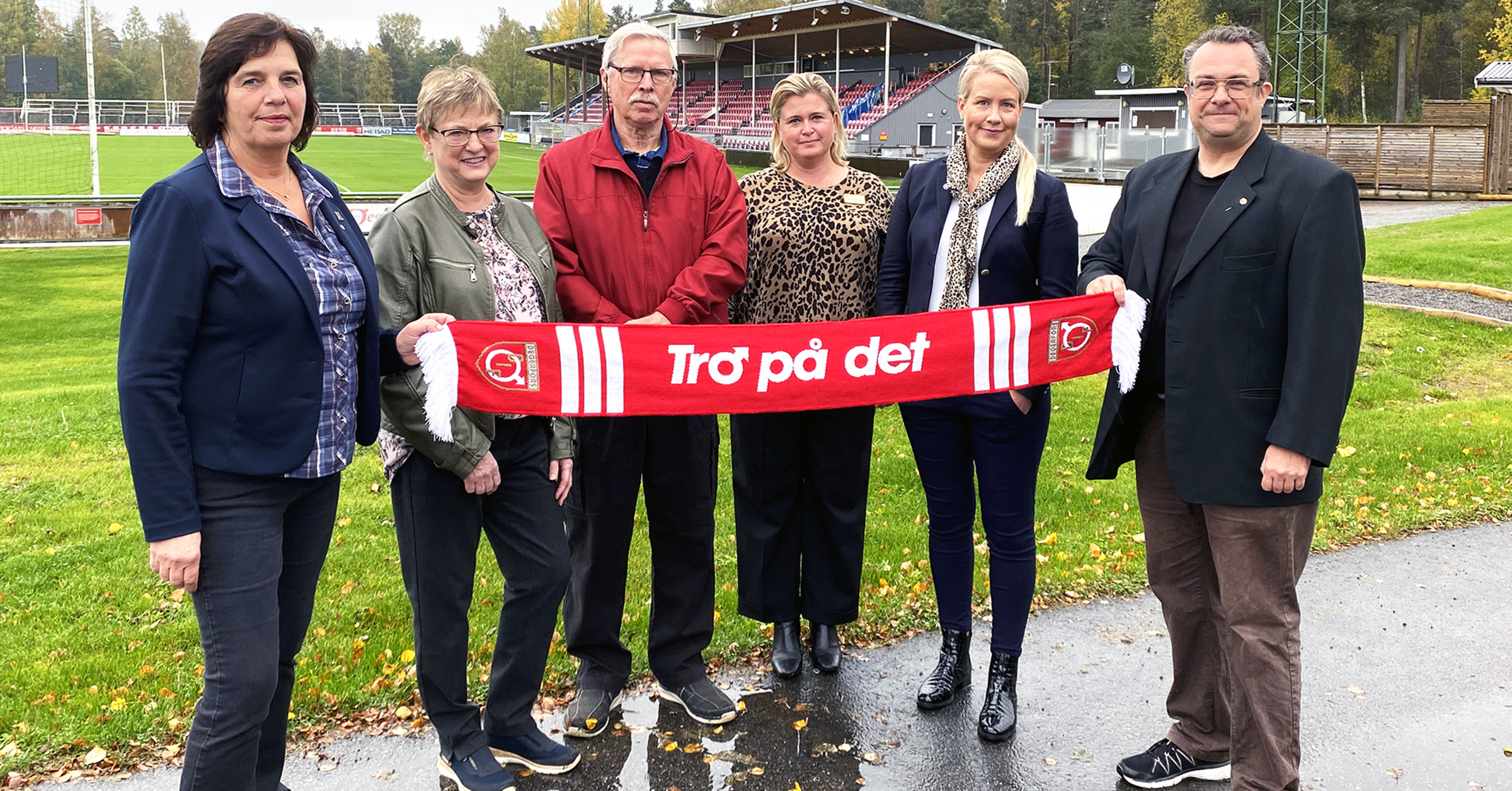 Degerfors kommuns politiska ledning håller tillsammans med Degerfors IFs ordförande i en röd-vit halsduk med texten Tro på det.