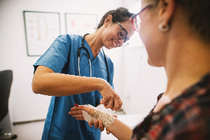 En sjuksköterska i blå uniform lindar ett bandage om en kvinnas arm.